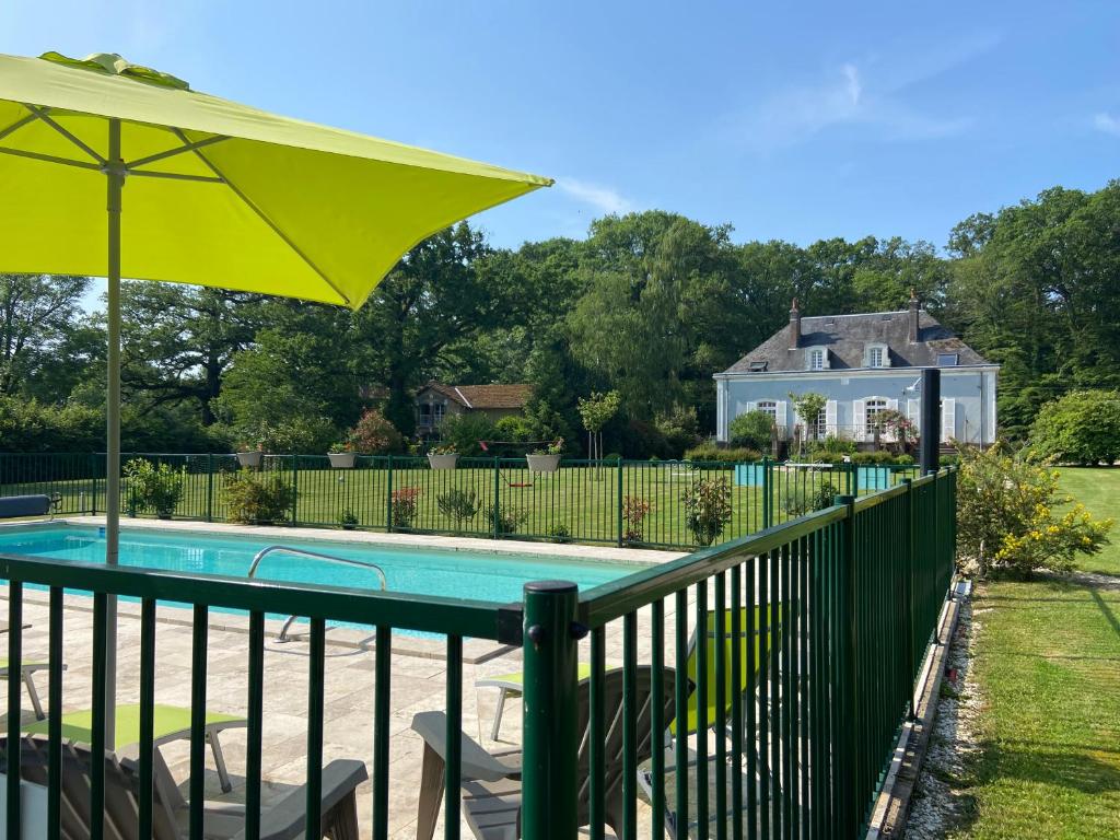 a pool with a fence and an umbrella at Hôtel les Grands Chênes in Saint-Fargeau