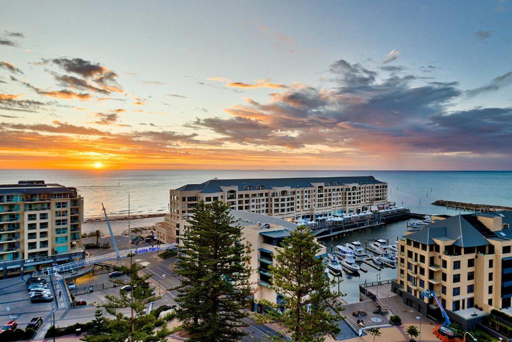 Una puesta de sol sobre un puerto con edificios y un puerto deportivo. en Belle Escapes - Glenelg Skyline Penthouse, en Glenelg