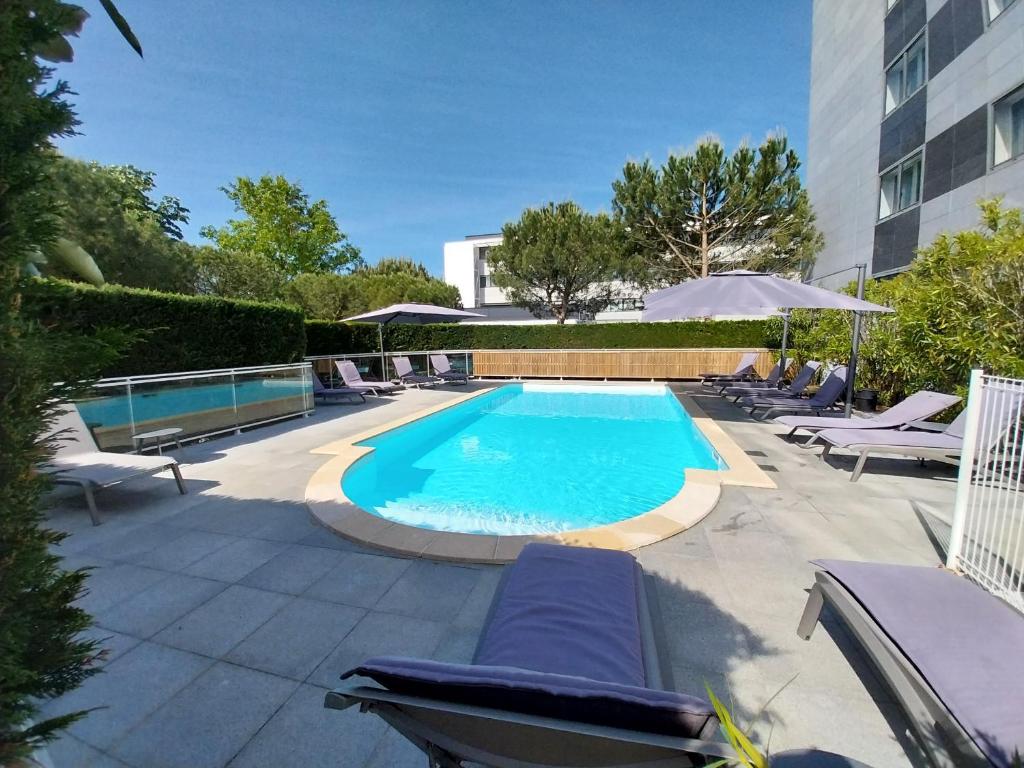 une piscine avec des chaises longues à côté d'un bâtiment dans l'établissement CERISE Bordeaux Mérignac Aéroport, à Mérignac