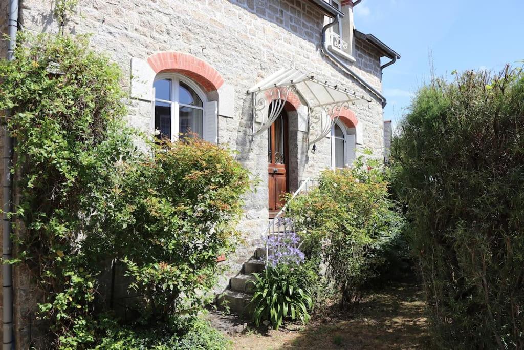 a stone house with a brown door and some bushes at Maison Dinannaise -Les Roses- in Dinan