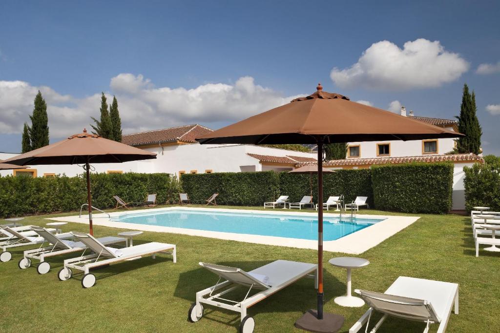 ein Pool mit Liegestühlen und Sonnenschirmen neben einem Gebäude in der Unterkunft AZZ Castellar Hacienda El Alcornocal in Castellar de la Frontera