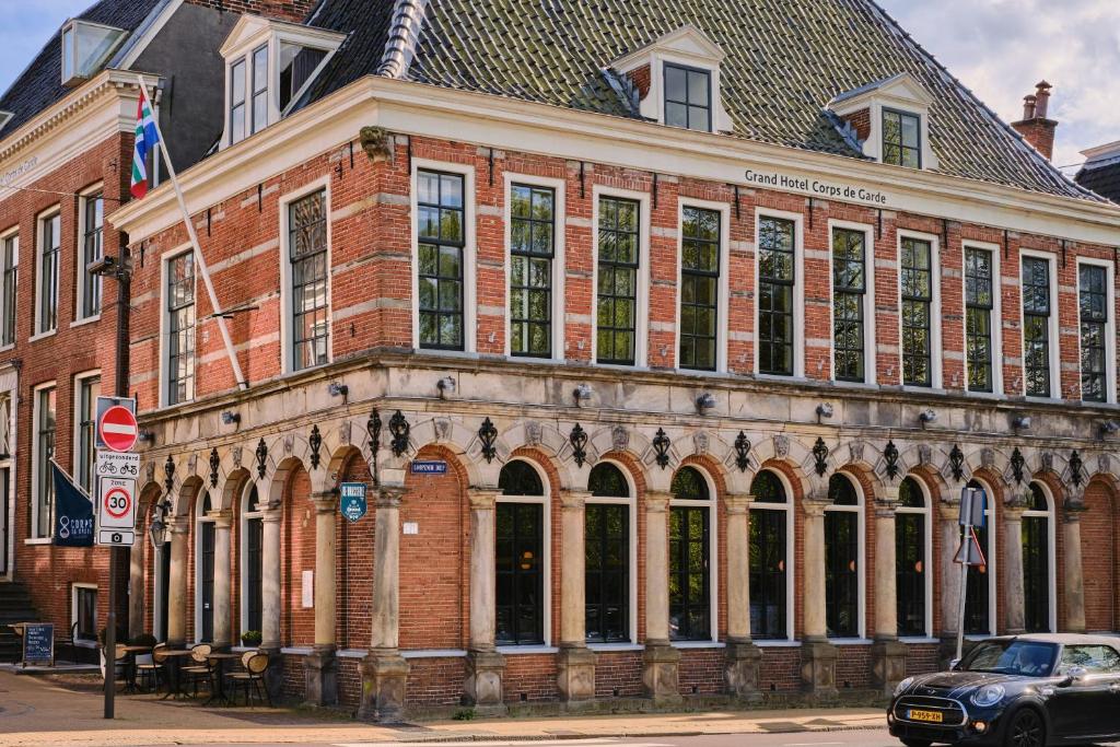 een groot bakstenen gebouw met een auto ervoor geparkeerd bij Hotel Corps de Garde in Groningen