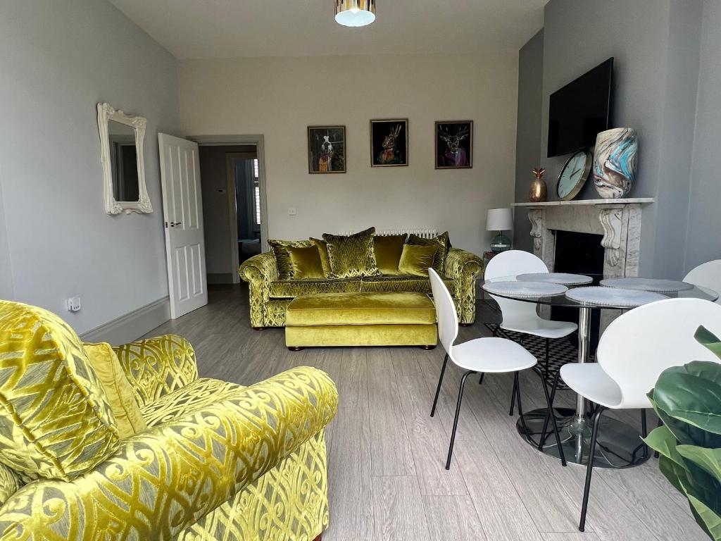 uma sala de estar com sofás amarelos, uma mesa e cadeiras em Linden Garden apartment em Bedford