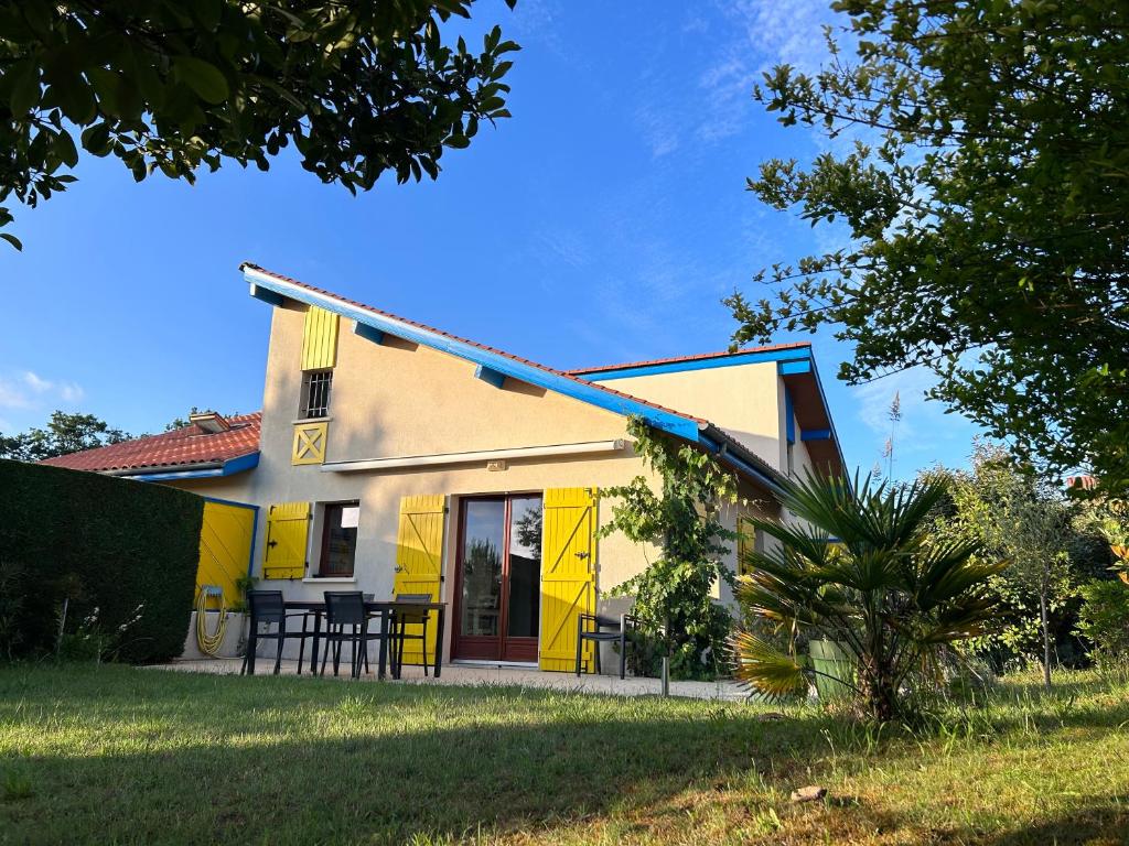 une maison jaune avec un toit bleu dans l'établissement Jolie maison de vacances avec terrasse et jardin, à Saint-Julien-en-Born