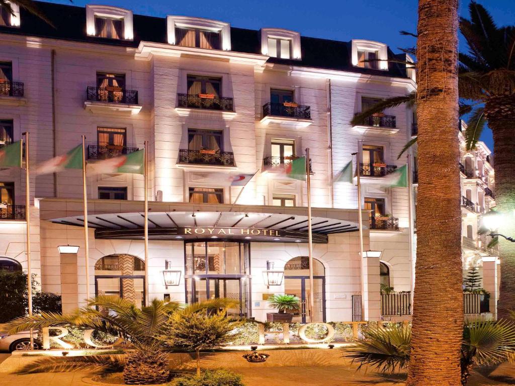 un bâtiment d'hôtel avec drapeaux devant lui dans l'établissement Royal Hotel Oran - MGallery Hotel Collection, à Oran