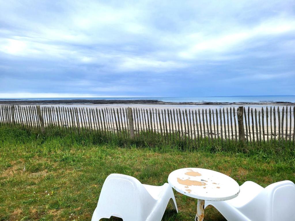 Dos sillas blancas y una mesa frente a un cuerpo de agua. en La Maison du Rivage, en Bretteville-sur-Ay