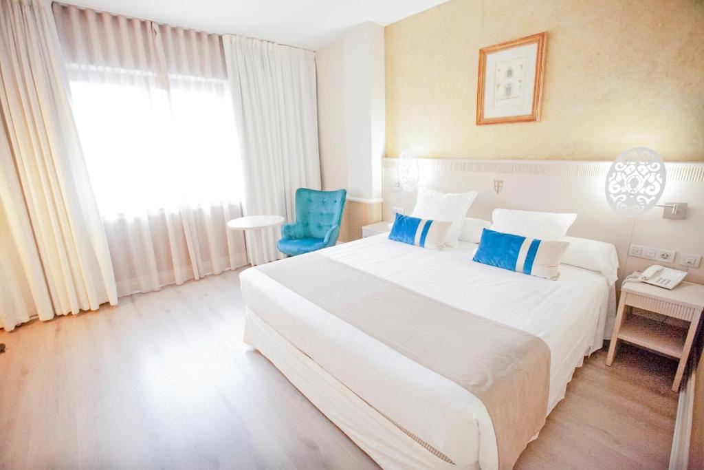 a bedroom with a large white bed and a blue chair at Hotel Alfonso VIII in Soria