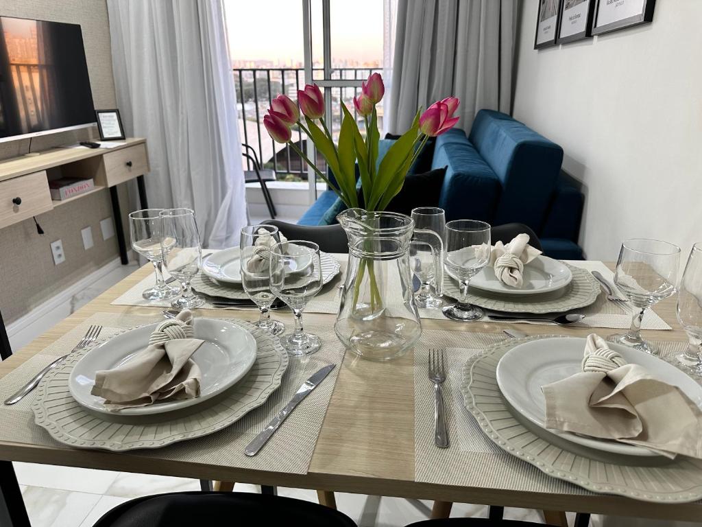 uma mesa de jantar com pratos, copos e flores em Apartamento novo decorado com sacada e linda vista da Cidade em São Paulo