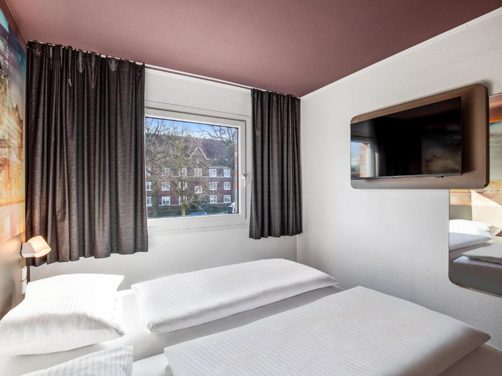 a bedroom with two beds and a tv and a window at B&B Hotel Hamburg-Airport in Hamburg