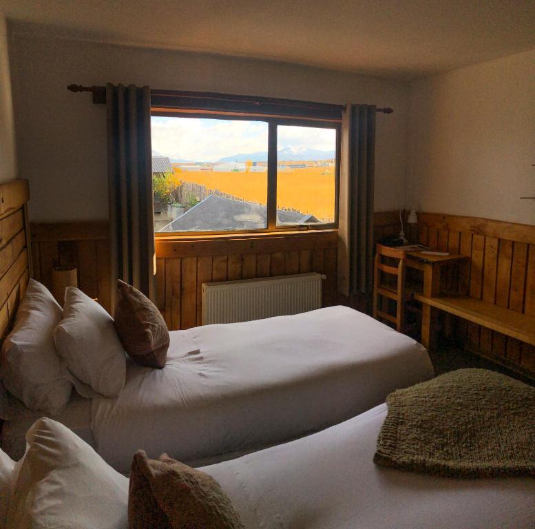 a bedroom with two beds and a large window at Weskar Lodge Hotel in Puerto Natales