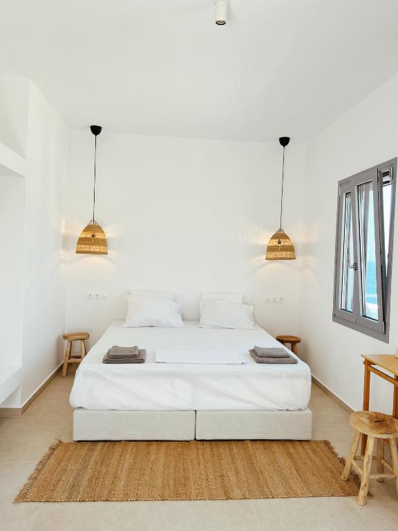 a white bedroom with a bed and two pendant lights at Theros (Θέρως) in Batsi
