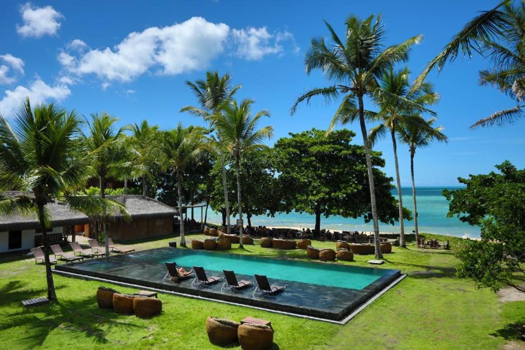 a resort with a pool and palm trees and the ocean at Pousada Cores do Mar Caraíva in Caraíva