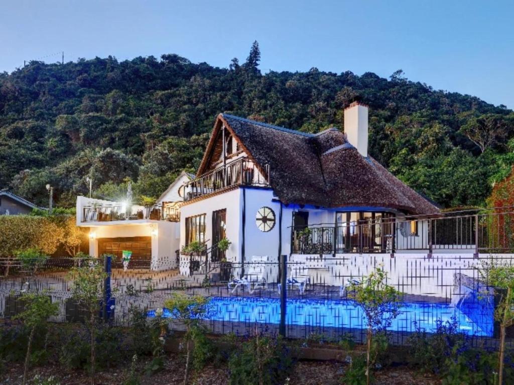 a house with a thatched roof and a swimming pool at Cloverleigh Guest House in Wilderness