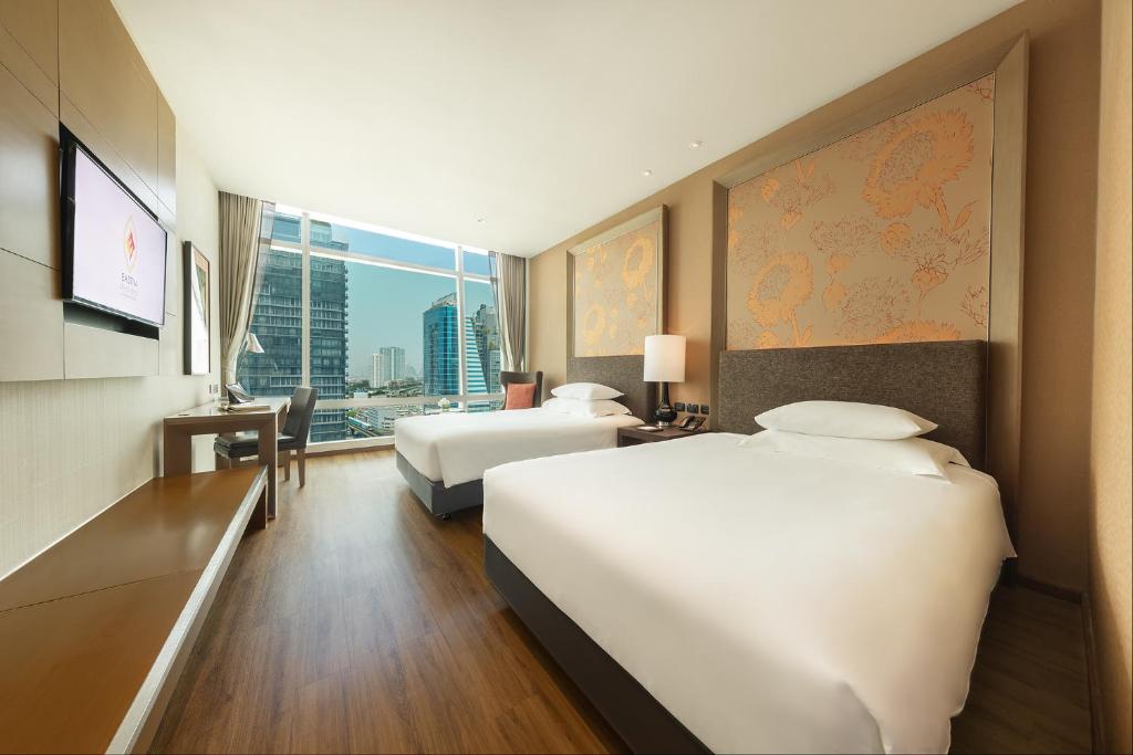 A twin room with two beds, a city-facing window and a built-in TV console.
