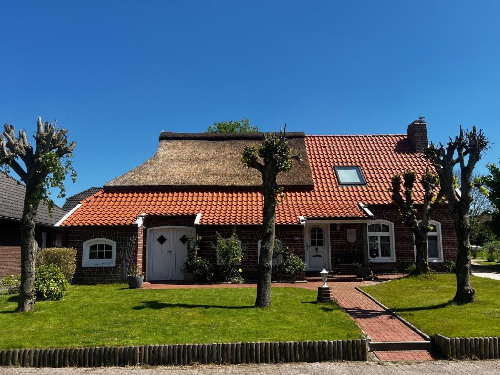 a house with a red roof and palm trees at Lindenhuus-Urlaub unter einem Teilreetdach-Terrasse - Nahe Norden-Norddeich in Osteel