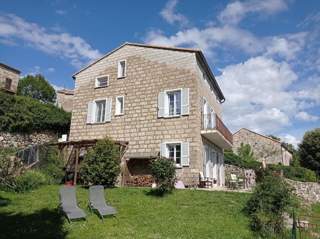 une grande maison en pierre avec 2 chaises dans la cour dans l'établissement Casa Sarrinca, à Serra-di-Scopamene