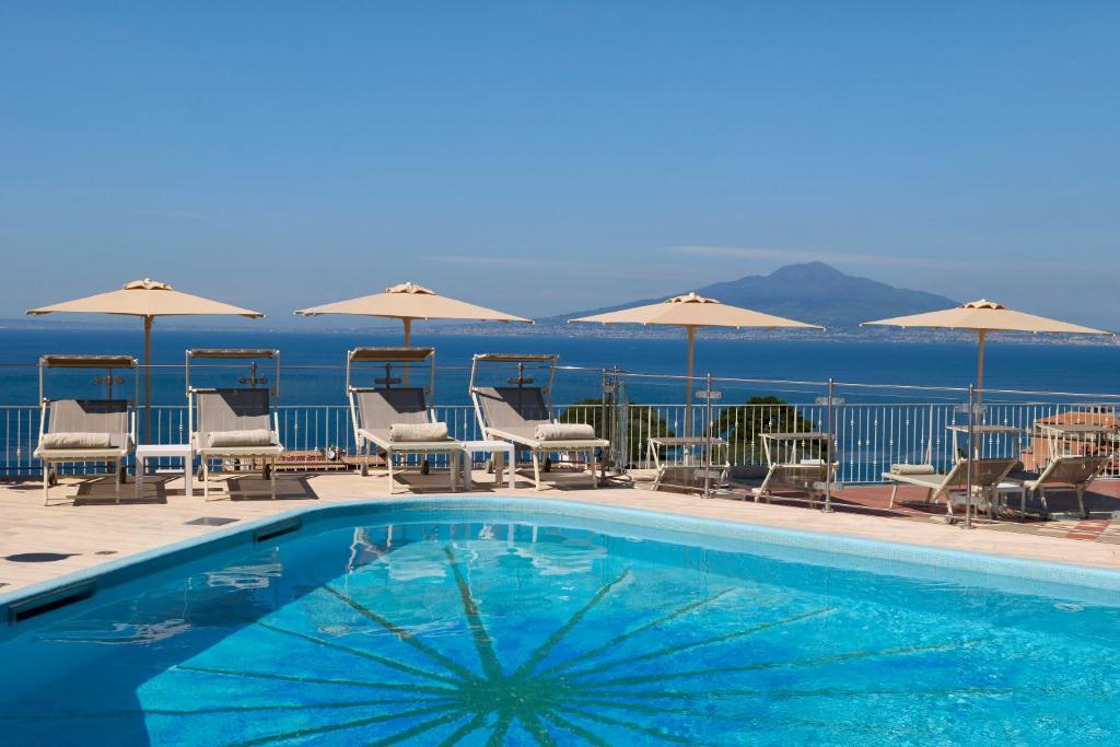 a swimming pool with chairs and umbrellas and the ocean at Grand Hotel de la Ville in Sorrento