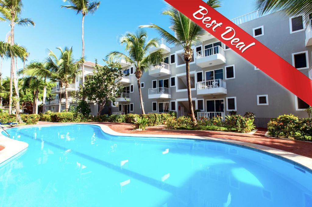 - une piscine en face d'un bâtiment avec des palmiers dans l'établissement TROPICANA SUITES DELUXE BEACH CLUB and POOL - playa LOS CORALES, à Punta Cana