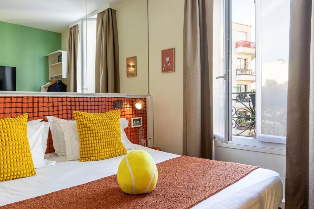 a bedroom with a bed with yellow pillows and a window at Hotel Olympic Paris Boulogne by Patrick Hayat in Boulogne-Billancourt