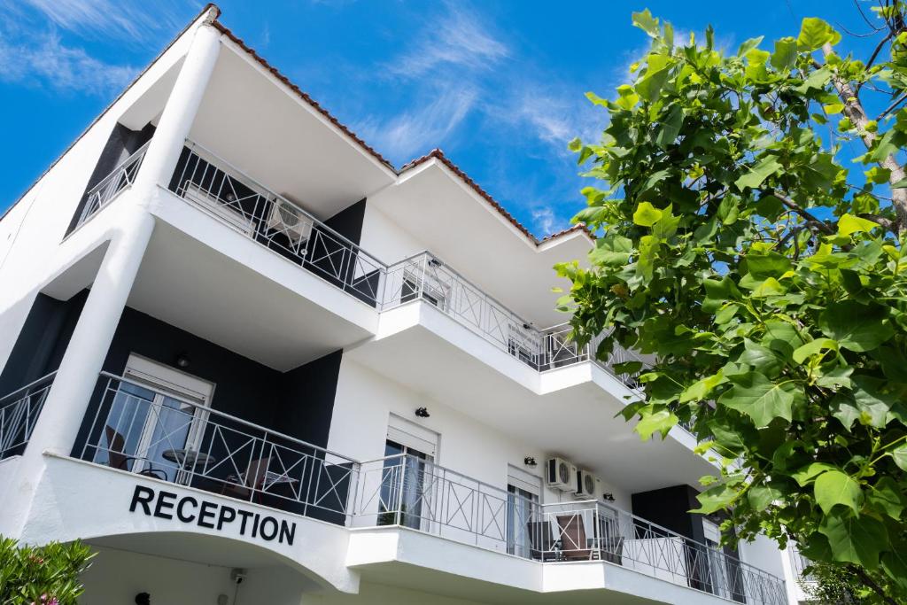 ein weißes Gebäude mit Balkonen und einem Baum in der Unterkunft DOMES APARTMENTS in Kallithea (Chalkidiki)