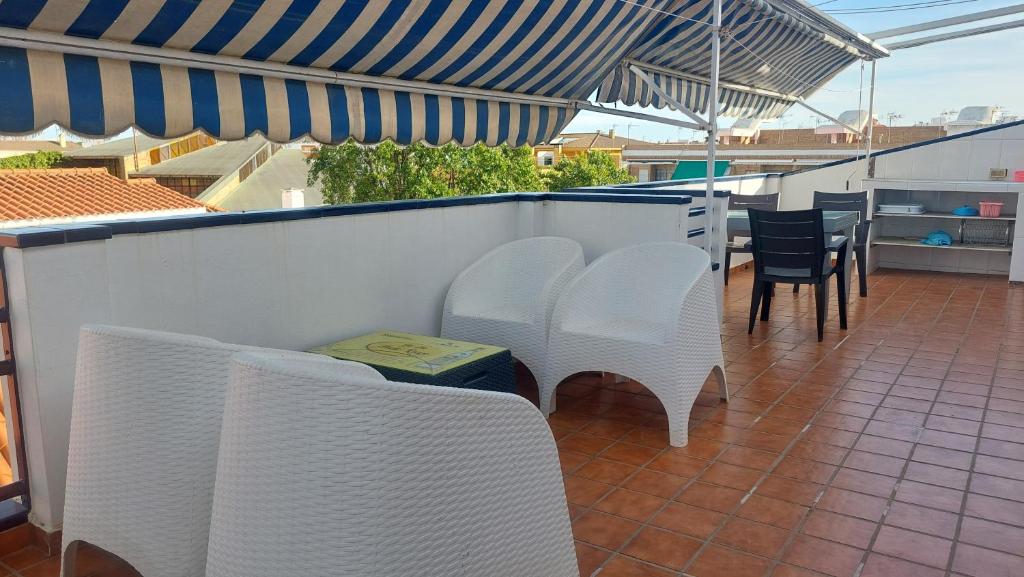 eine Terrasse mit weißen Stühlen, Tischen und einem Sonnenschirm in der Unterkunft UMBRIA Mar in Punta Umbría
