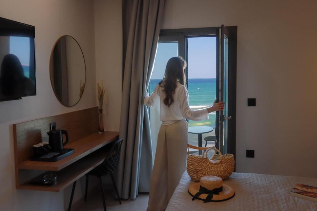 una mujer parada en una habitación de hotel mirando por la ventana en Tropical Beach A, en Amoudara Herakliou