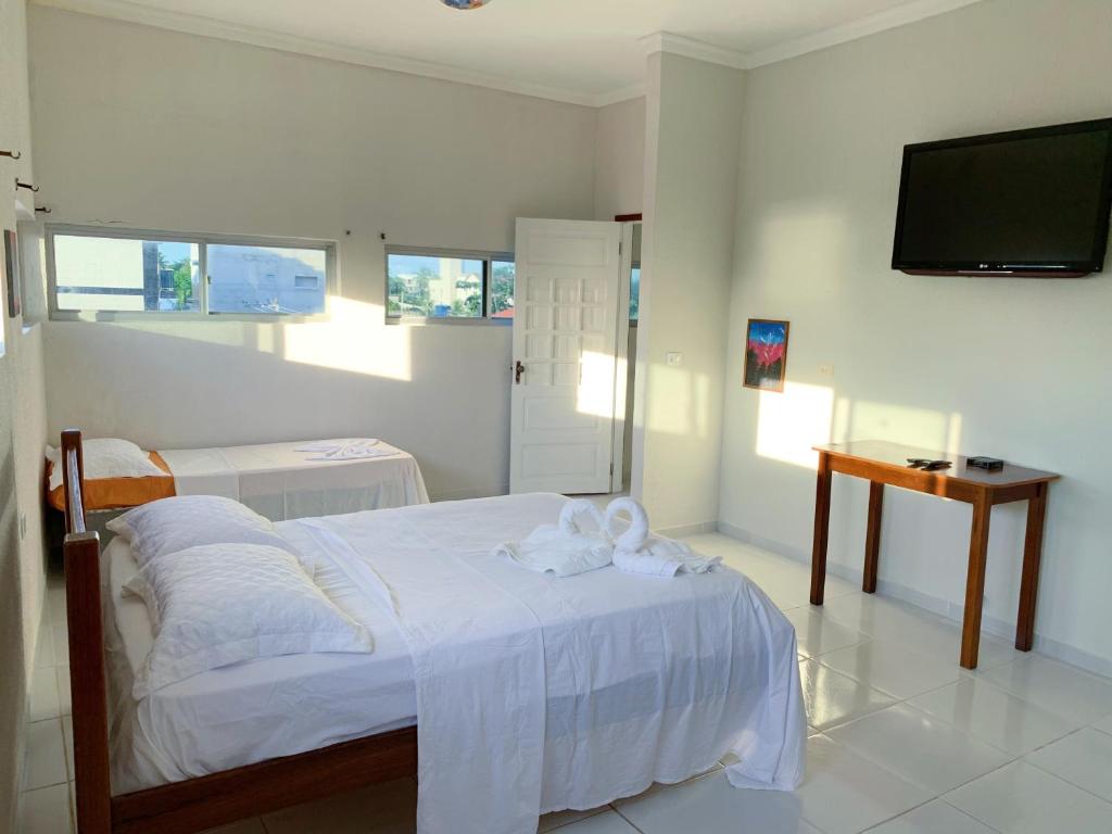 a white bedroom with a bed and a flat screen tv at Flats e Suítes Elcaline in Porto De Galinhas