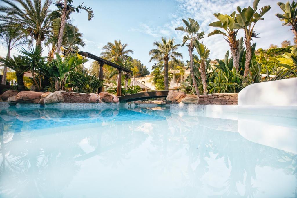 una piscina con agua azul y palmeras en Hotel Swiss Moraira, en Moraira