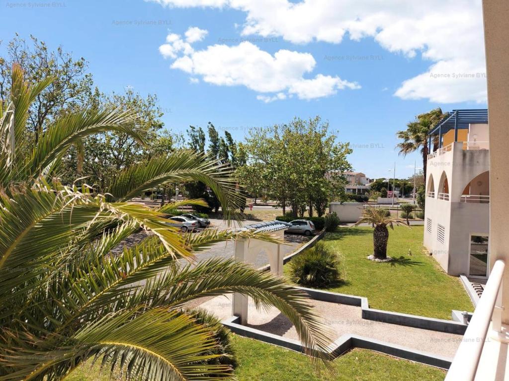 - une vue sur un parc avec des palmiers et un bâtiment dans l'établissement Résidence Natureva - Appartement T2 2 PERS. MAE-2701, au Cap d'Agde