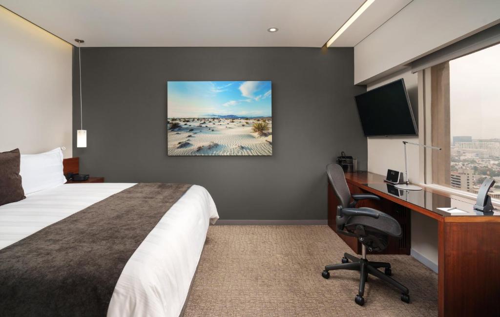 A bedroom workspace beside a window, with a bed and wall-mounted television.