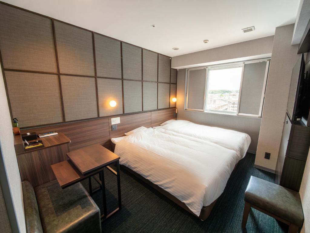 奈良市にあるスーパーホテルPremierJR奈良駅のベッド、デスク、窓が備わるホテルルームです。