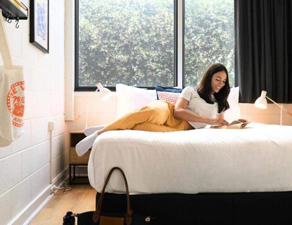 a woman sitting on a bed reading a book at The Village North Melbourne in Melbourne