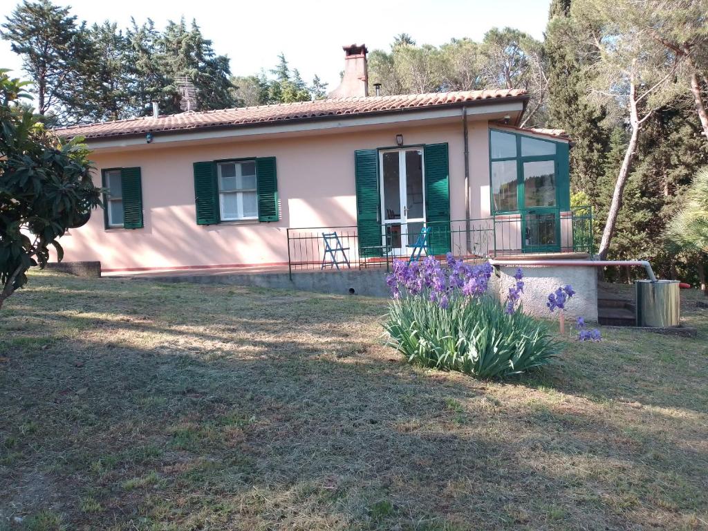 a small house with green windows and purple flowers at Piccolo appartamento immerso nella campagna in Rosignano Marittimo