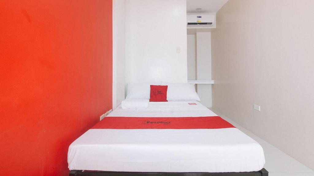 a white bed with a red pillow on top of it at RedDoorz @ Aerial Hotel Los Baños in Los Baños