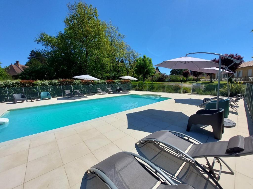 a swimming pool with chairs and an umbrella at Studios Les Courrèges in Vézac