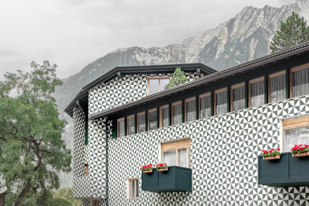 un edificio con fiori alle finestre e montagne sullo sfondo di Hotel Drumlerhof a Campo Tures