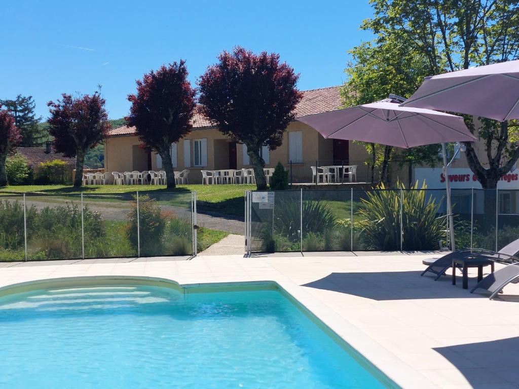 a swimming pool with an umbrella next to a house at Gîtes Les Courrèges in Vézac