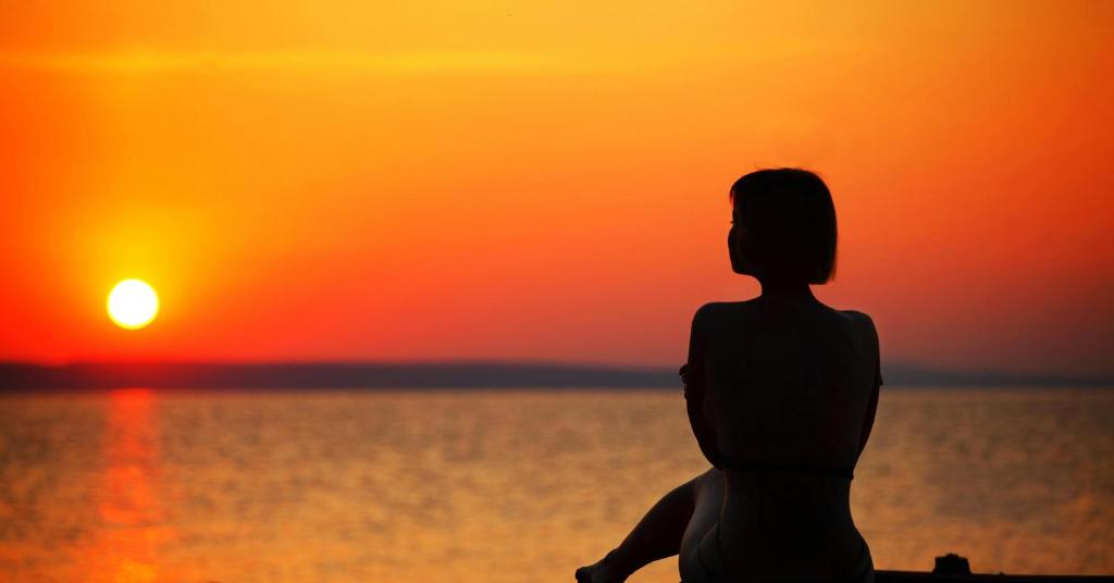 una mujer sentada en la playa mirando la puesta de sol en Hilltop Serenity Villa, en Imerovigli