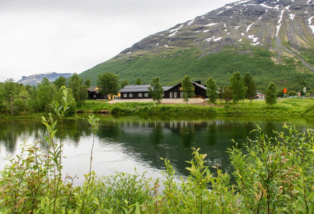 una casa junto a un lago con una montaña en el fondo en Vollan Gjestestue, en Nordkjosbotn