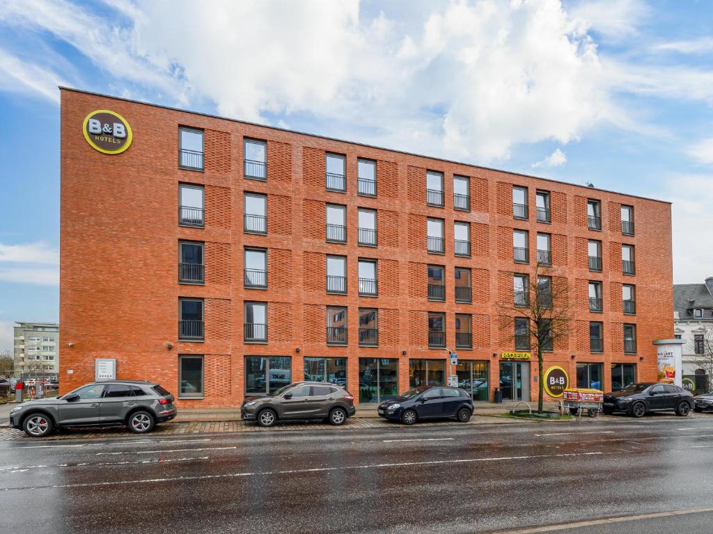 ein Backsteingebäude mit Autos auf einem Parkplatz in der Unterkunft B&B Hotel Bremerhaven in Bremerhaven