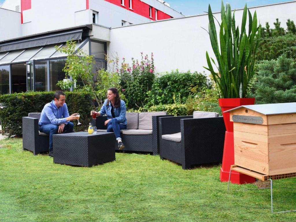 two people sitting on chairs in a garden at Ibis Nantes la Beaujoire Parc Expo in Nantes