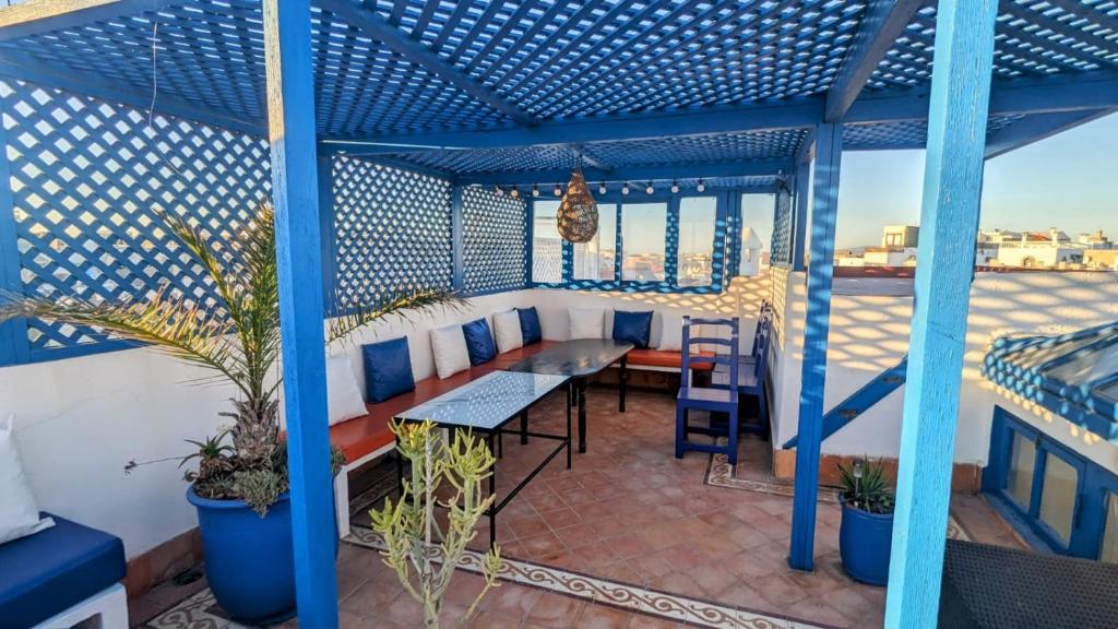 a balcony with a blue pergola with a table and chairs at La Maison Du Vent in Essaouira