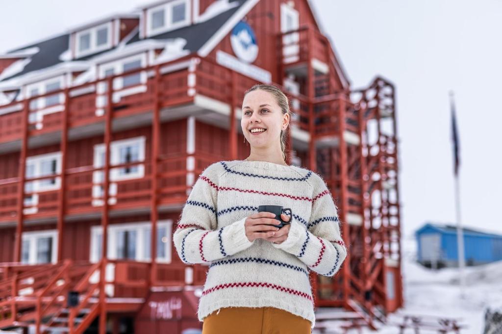 a woman standing in front of a building holding a cell phone at HOTEL SØMA Ilulissat in Ilulissat