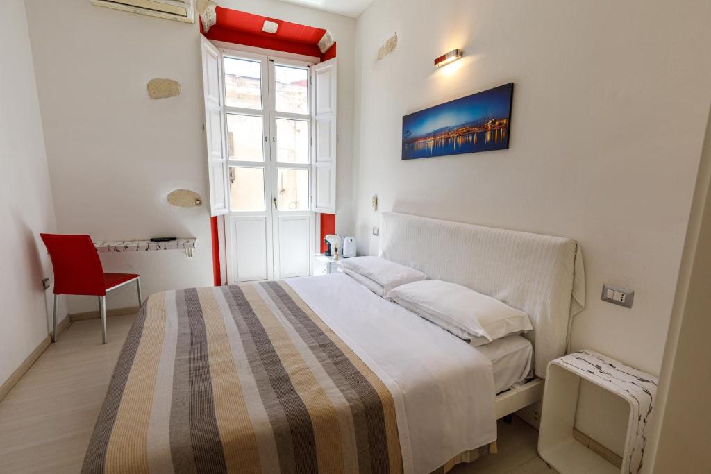 a white bedroom with a bed and a red chair at Onlyrooms II - Old Town & Typical Food in Cagliari