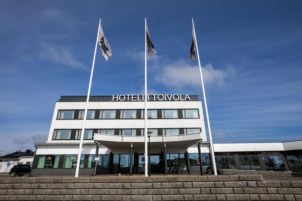 um hotel com três bandeiras em frente a um edifício em Hotelli Toivola em Kemi