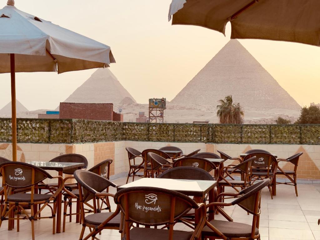 uma fila de mesas e cadeiras com pirâmides ao fundo em Hur magic inn em Cairo