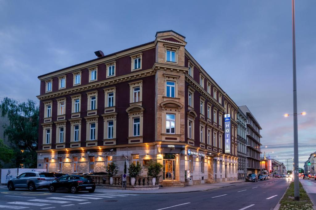 un grand bâtiment en briques avec des voitures garées devant lui dans l'établissement Best Western Hotel Strasser, à Graz