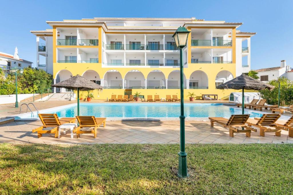 un hotel con una piscina con sillas y sombrillas en Apartamentos Turisticos Alagoa Praia en Altura