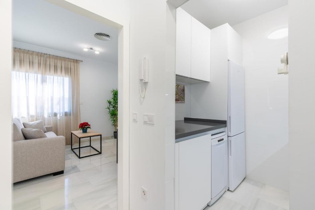 Una cocina blanca y una sala de estar con un sofá. en APARTAMENTOS FIBES GARDEN SEVILLA, en Sevilla