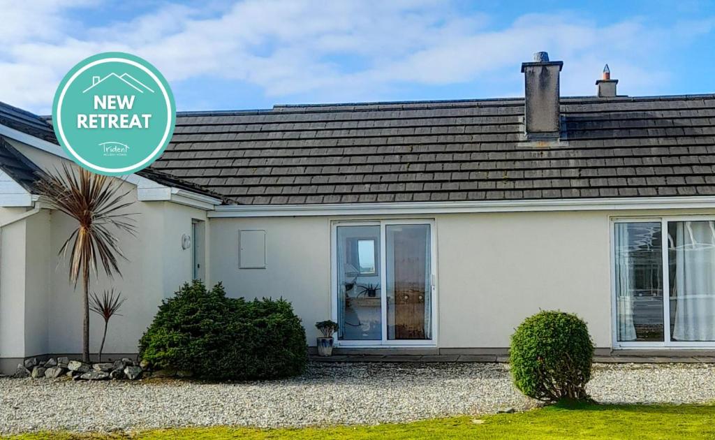 a white house with a new retreat sign in front of it at Ballyconneely Holiday Home No 5 by Trident Holiday Homes in Ballyconneely